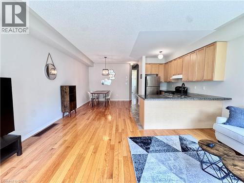 Open-concept living space featuring wood-finish flooring, a kitchen with light wood cabinetry, a breakfast bar with stone countertop, stainless steel refrigerator, and a dining area with pendant light - 110 Highland Road E Unit# 53, Kitchener, ON - Indoor Photo Showing Living Room