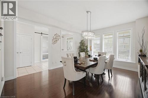 Hardwood flooring extends throughout this space, complemented by a contemporary chandelier and a wall of three windows with blinds - 58 Doon Creek Street, Kitchener, ON - Indoor Photo Showing Dining Room