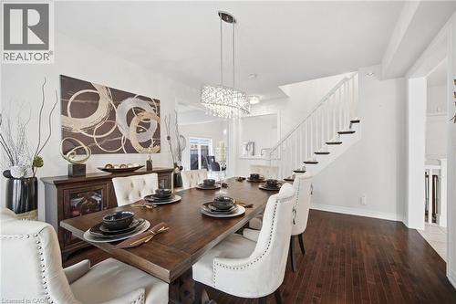 Formal dining space featuring dark wood-finish flooring and a contemporary crystal chandelier - 58 Doon Creek Street, Kitchener, ON - Indoor Photo Showing Dining Room