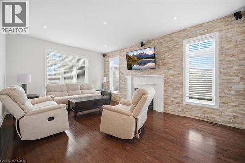 Living area featuring wood-finish flooring, a stone-accented wall, white window blinds, a built-in fireplace with a white mantel, and recessed lighting - 58 Doon Creek Street, Kitchener, ON - Indoor Photo Showing Living Room With Fireplace