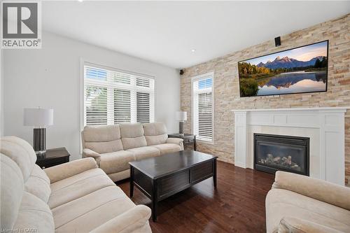 Living area featuring a stone accent wall with a fireplace and white mantel, dark wood-finish flooring, and multiple windows - 58 Doon Creek Street, Kitchener, ON - Indoor Photo Showing Living Room With Fireplace