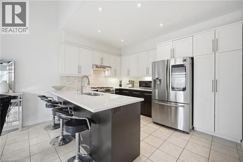 Contemporary kitchen featuring a large central island with seating, white shaker cabinetry, stainless steel appliances, and light-toned tile flooring - 58 Doon Creek Street, Kitchener, ON - Indoor Photo Showing Kitchen With Double Sink With Upgraded Kitchen