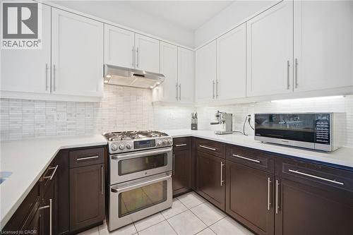 Kitchen featuring two-tone cabinetry with white upper and dark wood-finish lower cabinets, stone countertops, and a full-height tile backsplash - 58 Doon Creek Street, Kitchener, ON - Indoor Photo Showing Kitchen With Upgraded Kitchen