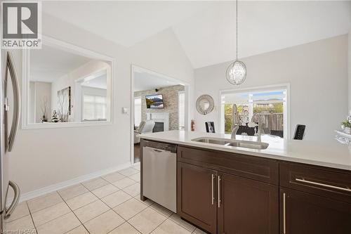 Kitchen featuring dark wood cabinetry, light-toned countertops, a double basin sink with a high-arc faucet, and stainless steel dishwasher - 58 Doon Creek Street, Kitchener, ON - Indoor Photo Showing Kitchen With Double Sink