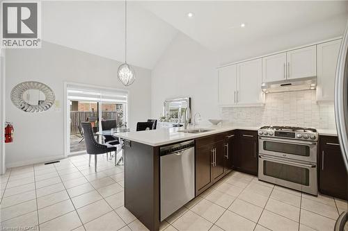 Kitchen featuring white tile flooring, two-tone cabinetry, stainless steel appliances, and a white countertop island with an undermount sink - 58 Doon Creek Street, Kitchener, ON - Indoor Photo Showing Kitchen With Upgraded Kitchen