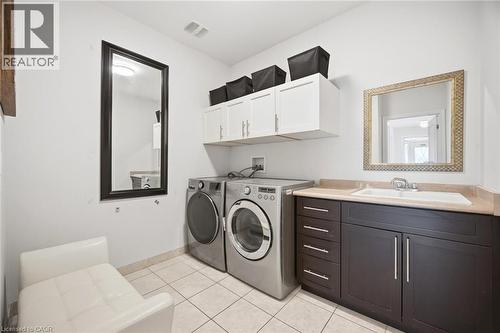 Utility room featuring a built-in sink with dark wood-finish cabinetry, a light-toned countertop, white upper storage cabinets, and tiled flooring - 58 Doon Creek Street, Kitchener, ON - Indoor Photo Showing Laundry Room