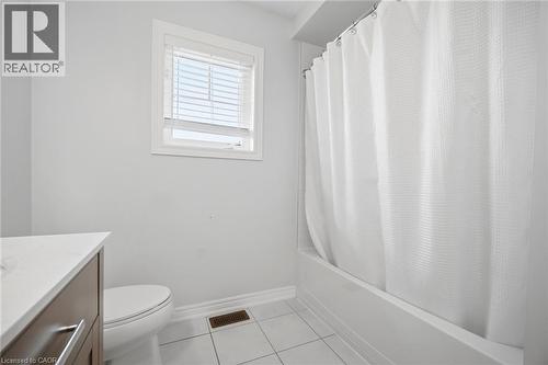 Bathroom featuring a white bathtub with shower, white tiled flooring, a window with white blinds, and a wood-finish vanity with a white countertop - 58 Doon Creek Street, Kitchener, ON - Indoor Photo Showing Bathroom