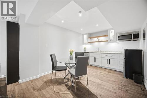 Contemporary kitchen area featuring white cabinetry with dark hardware, stone-finish countertops, wood-finish flooring, and recessed lighting - 58 Doon Creek Street, Kitchener, ON - Indoor
