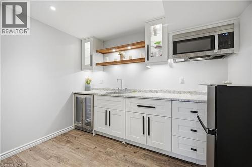 Built-in wet bar featuring white cabinetry, a stainless steel under-counter beverage cooler, an undermount sink with a gooseneck faucet, light-toned countertops, and wood-finish flooring - 58 Doon Creek Street, Kitchener, ON - Indoor Photo Showing Kitchen