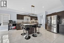 Kitchen featuring a central island with countertop seating, dark wood-finish cabinetry, a white subway tile backsplash, and a side-by-side stainless steel refrigerator - 