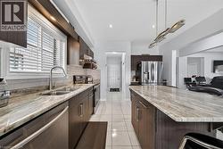 Kitchen featuring dark wood-finish cabinetry, light-toned tiled flooring, stainless steel appliances, marble-look countertops, and a subway tile backsplash - 