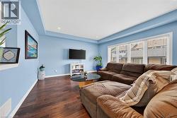 Spacious living area featuring rich wood-finish flooring, a large multi-pane window, recessed ceiling lighting, a contemporary tray ceiling, and a clean white baseboard trim - 