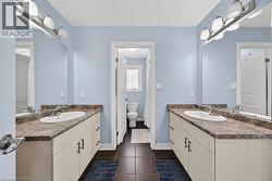 Dual vanity sinks with laminate countertops, light cabinetry, and dark tile flooring - 