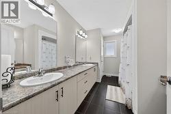 Spacious bathroom featuring a dual vanity with undermount sinks, granite-finish countertops, extensive cabinet storage, dark floor tiling, and a window providing natural light - 