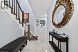 Bright entryway featuring light-toned tile flooring, a staircase with wood balusters and carpeted treads, and a decorative archway - 