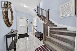 Bright entryway featuring white tile flooring, a white paneled door with glass insert, and a carpeted staircase with wood handrail and iron balusters - 