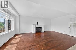 Spacious room featuring wood-finish flooring, a prominent fireplace with a white mantel, and a large window with blinds - 