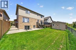 Expansive green space featuring a large wooden shed, rear deck with dark railings, and a concrete patio - 