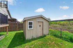 Backyard storage shed with a panel door and a single window, positioned on a grassy area with a chain-link fence - 