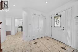 Entryway featuring light-toned tile flooring with decorative accents, a white paneled door with an ornate glass insert, and white louvered side panels - 