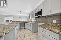 Kitchen featuring granite countertops, light cabinetry, tile flooring, a subway tile backsplash, and stainless steel appliances - 