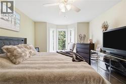 Room with light-toned walls, featuring a bay window with three vertical windows, a ceiling fan with light fixture, and wood-finish flooring - 
