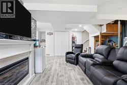 Finished lower level featuring wood-finish flooring, a white mantel with an electric fireplace, a stone-look accent wall, and bi-fold closet doors - 