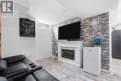 Living area featuring wood-finish flooring, a stone-accented wall, and a built-in electric fireplace with a white mantel - 