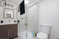 Contemporary bathroom featuring a glass-enclosed shower with white tiled walls, a dark wood-finish vanity with an integrated sink, and a framed mirror with overhead lighting - 