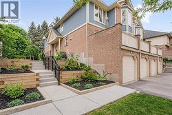 Multi-story townhome exterior featuring brick and siding, multiple garage bays, a prominent bay window, and a terraced walkway with landscaping - 