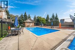 Outdoor swimming pool with concrete surround, adjacent brick pool house, and a fenced tennis court - 