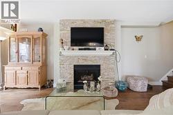 Living area featuring a floor-to-ceiling stacked stone fireplace with a white mantel, a built-in fireplace insert, and rich wood-finish flooring - 