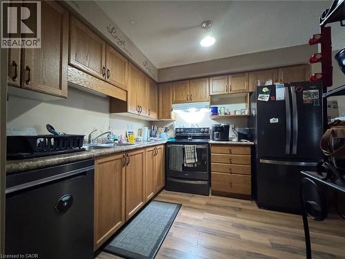 Kitchen featuring wood-finish flooring, wood cabinetry with dark hardware, a stainless steel sink, and a dark countertop - 517 Northbrook Place, Kitchener, ON - Indoor Photo Showing Kitchen With Double Sink