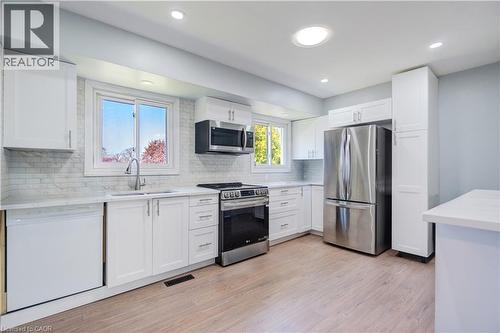 Modern kitchen featuring white shaker-style cabinetry, stainless steel appliances, a white tile backsplash, light-toned wood-finish flooring, and recessed lighting - 100 Lauris Avenue, Cambridge, ON - Indoor Photo Showing Kitchen With Upgraded Kitchen