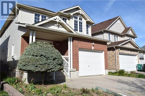 Brick and siding exterior featuring a covered porch with white railings, a front-facing dormer with multiple windows, and an attached two-car garage with a paved driveway - 28 Lemon Grass Street, Kitchener, ON - Outdoor