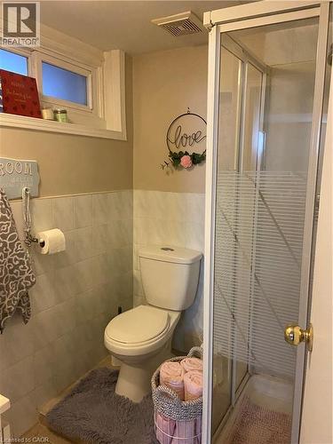 Bathroom featuring a white toilet, partial wall tiling, and a glass-enclosed shower stall - 52 Emerson Street, Hamilton, ON - Indoor Photo Showing Bathroom