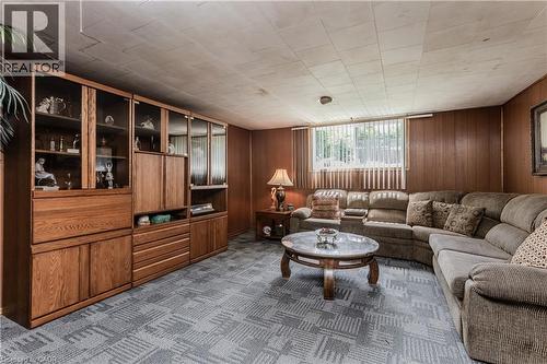 Spacious lower level featuring wood-finish paneling, a large built-in storage unit with glass-fronted cabinetry, and patterned carpeting - 643 Artreva Crescent, Burlington, ON - Indoor Photo Showing Living Room