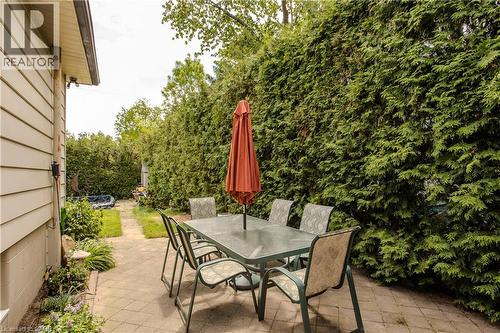 Paved patio area with a privacy hedge, bordered by the property's siding and a garden bed - 643 Artreva Crescent, Burlington, ON - Outdoor With Deck Patio Veranda