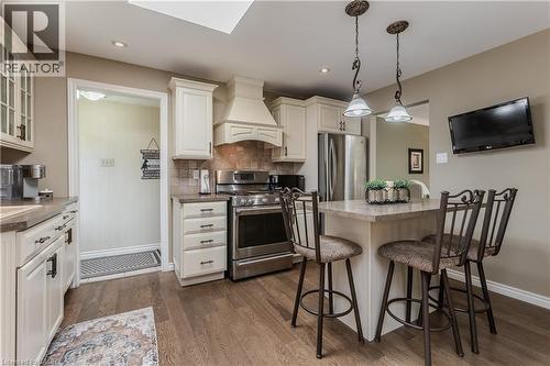 Kitchen featuring warm wood-finish flooring, light-toned cabinetry, stainless steel appliances, a built-in range hood, and a functional island with pendant lighting - 643 Artreva Crescent, Burlington, ON - Indoor Photo Showing Kitchen With Stainless Steel Kitchen With Upgraded Kitchen