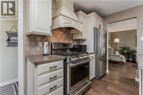 Gourmet kitchen featuring a stainless steel gas range, coordinating stainless steel refrigerator, cream cabinetry, stone-finish countertops, and a tiled backsplash - 643 Artreva Crescent, Burlington, ON - Indoor Photo Showing Kitchen