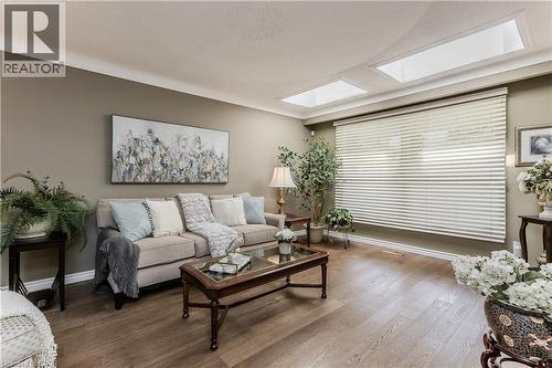Living area featuring wood-finish flooring, two rectangular skylights, a large window with horizontal blinds, and crown molding - 643 Artreva Crescent, Burlington, ON - Indoor Photo Showing Living Room