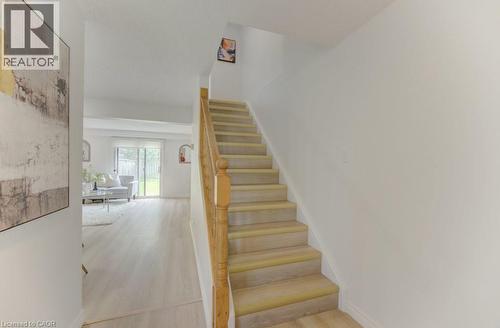 Carpeted staircase with wood-finish handrail and balusters, featuring light wood-finish flooring extending to a spacious living area with sliding glass doors opening to a fenced backyard - 603 Pinerow Crescent Unit# B, Waterloo, ON 