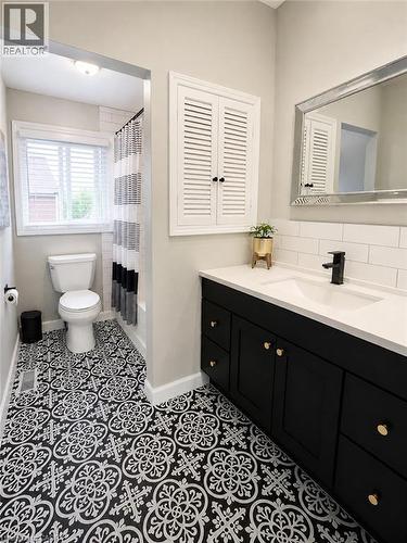 Bathroom featuring patterned black and white floor tiles, a black vanity with gold hardware, a white countertop with an integrated sink, a black faucet, and a white subway tile backsplash - 241 Thorner Drive, Hamilton, ON - Indoor Photo Showing Bathroom