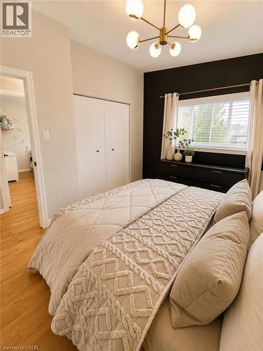Spacious room featuring wood-finish flooring, a contemporary six-light chandelier, a window with horizontal blinds, and bi-fold closet doors - 241 Thorner Drive, Hamilton, ON - Indoor Photo Showing Bedroom