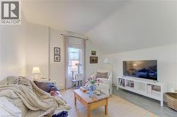 Attic living space featuring a window with natural light, light-toned walls, wood-finish flooring, and a sloped ceiling - 