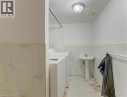Shared laundry space featuring a pedestal sink, a ceiling-mount light fixture, and tiled flooring - 