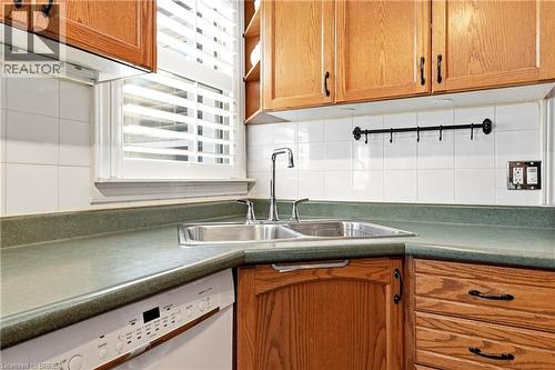 Kitchen featuring wood cabinetry, a double basin stainless steel sink with a chrome faucet, and a white tile backsplash - 23 Britannia Avenue, Hamilton, ON - Indoor Photo Showing Kitchen With Double Sink