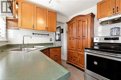 Kitchen featuring light wood cabinetry, a stainless steel double-basin sink with a chrome faucet, light green countertops, and a white tiled backsplash - 23 Britannia Avenue, Hamilton, ON - Indoor Photo Showing Kitchen With Double Sink