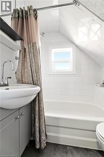 Bathroom featuring a pedestal sink with chrome faucet, a built-in bathtub, and white square tile walls - 23 Britannia Avenue, Hamilton, ON - Indoor Photo Showing Bathroom