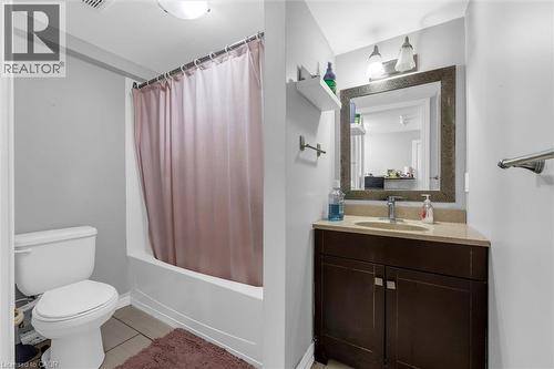 Bathroom featuring a white toilet, built-in bathtub with shower, dark wood-finish vanity, light-toned countertop, and framed mirror with integrated lighting - 46 Beaconsfield Drive, Hamilton, ON - Indoor Photo Showing Bathroom
